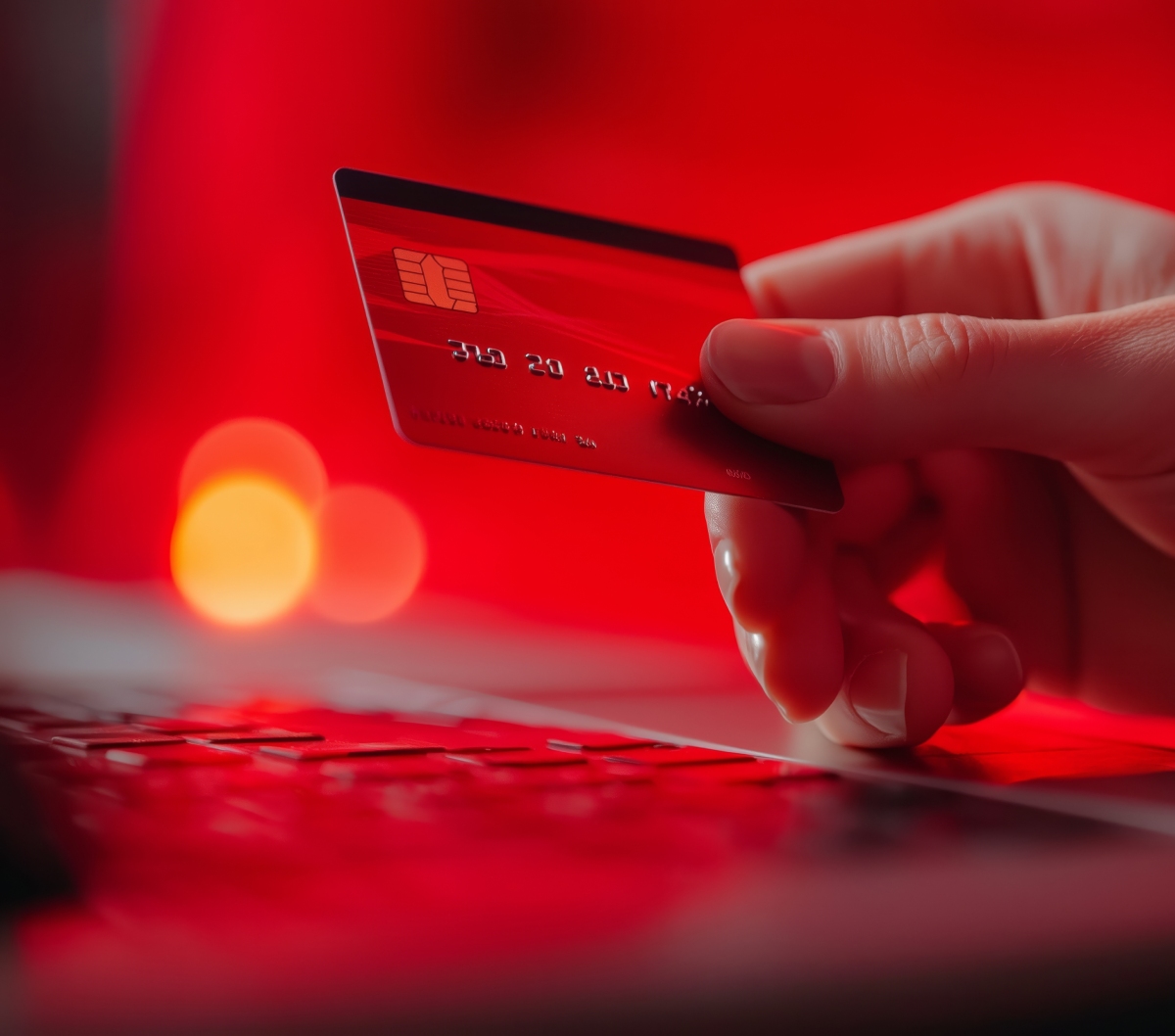 Main tenant une carte bancaire rouge au-dessus d'un clavier pour un paiement en ligne.