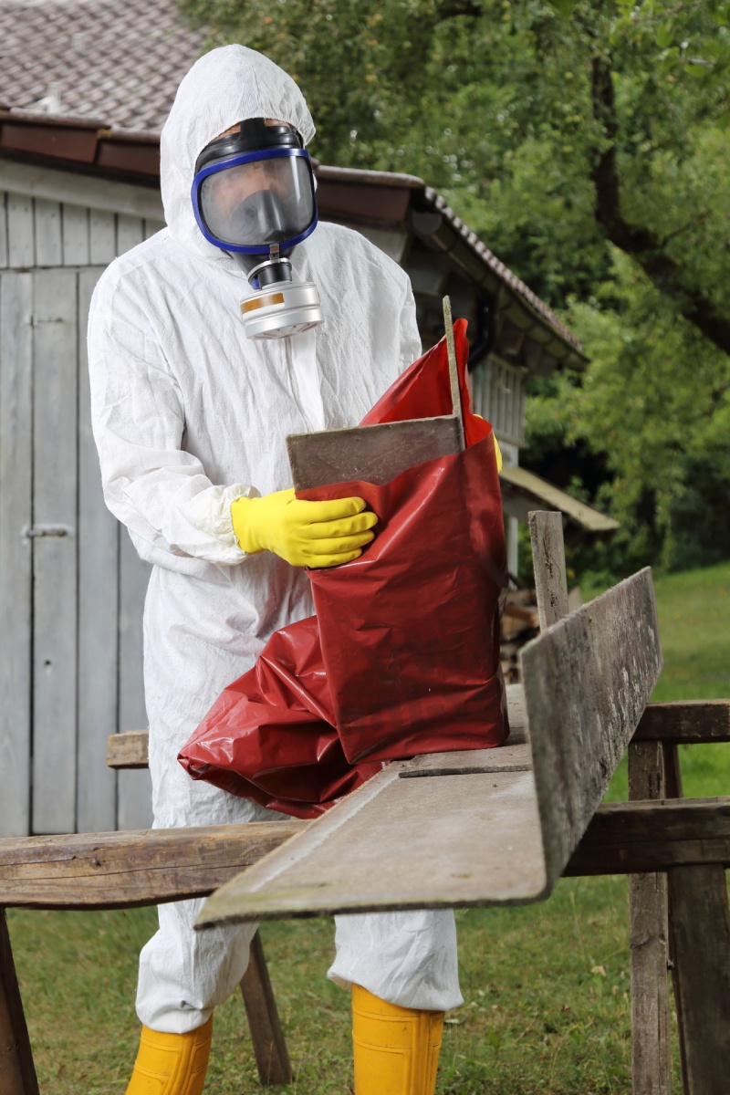 Opérateur en combinaison de protection manipulant des plaques d'amiante dans un sac de déchets.